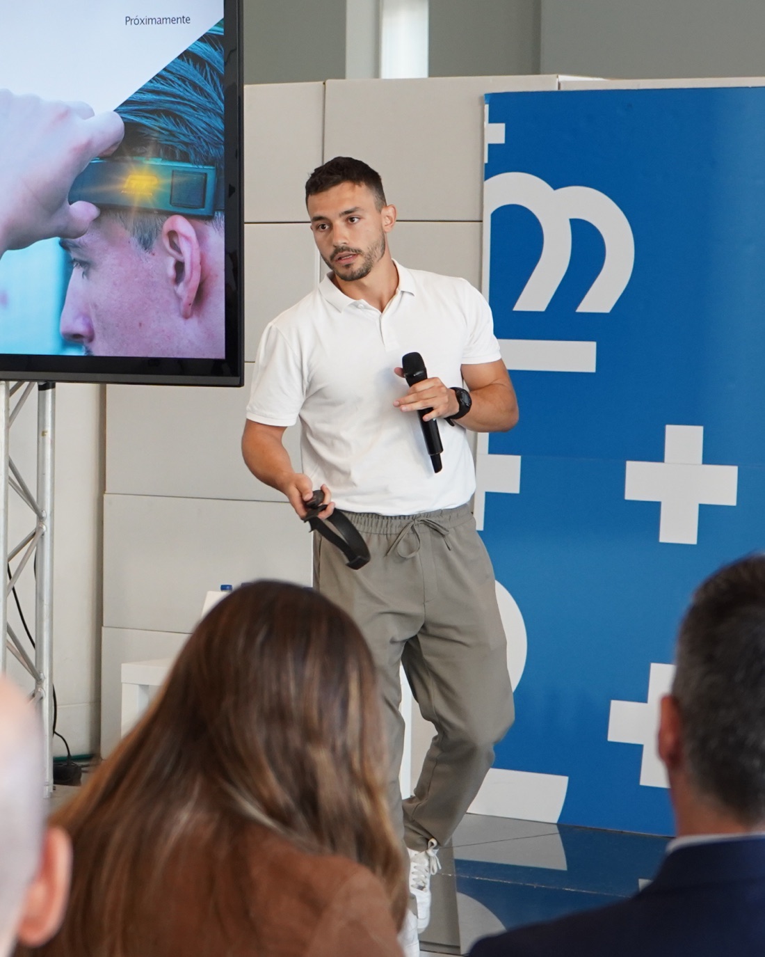 Rodrigo Ispierto presentando en un evento, micrófono en mano, junto a un panel de marca azul.